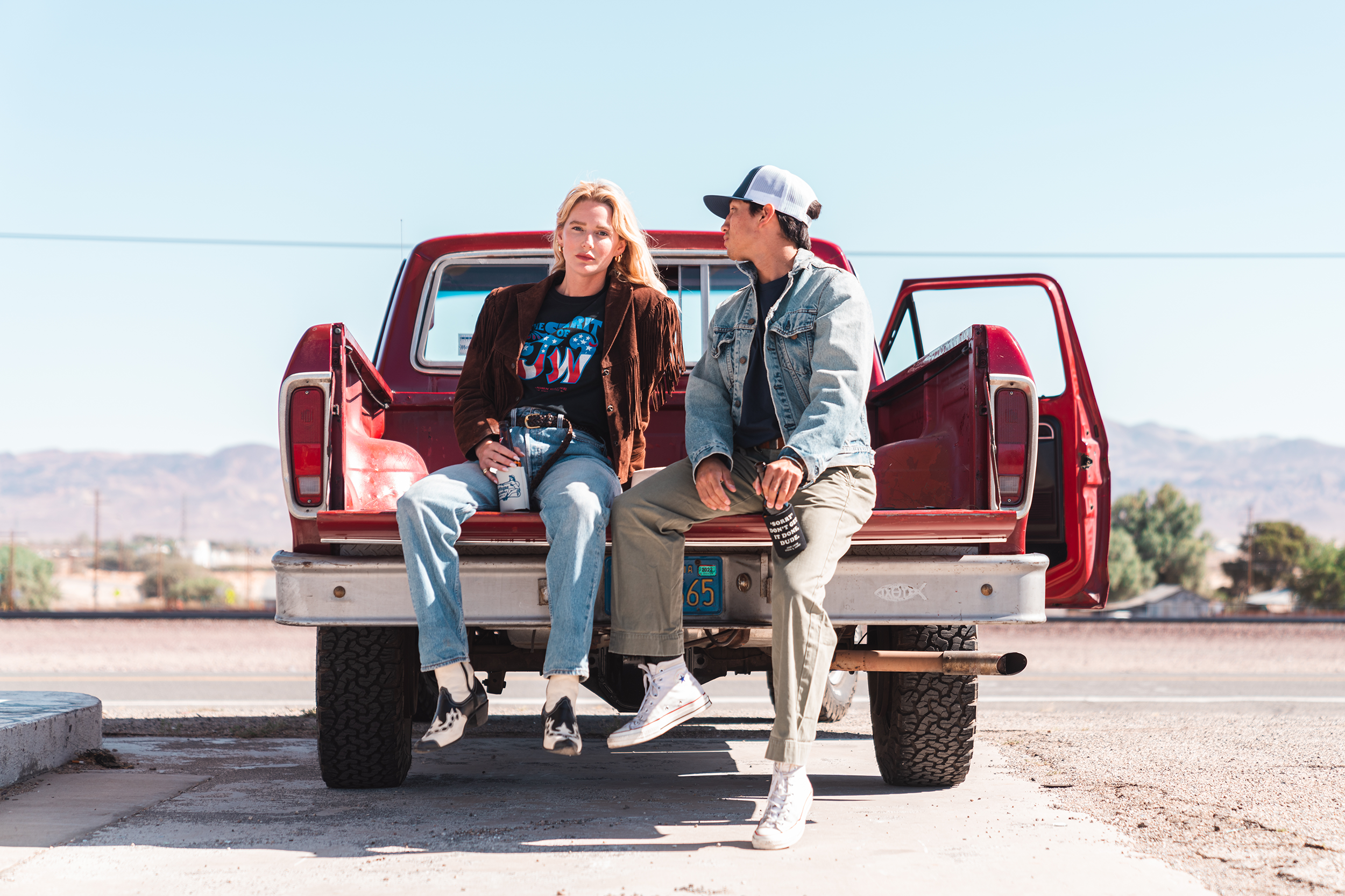 woman wearing john wayne tee on bed of truck next to man