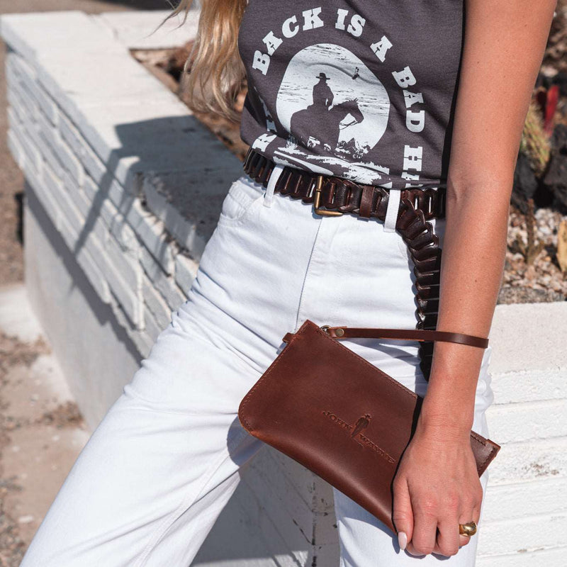 woman holding leather clutch with John Wayne silhouette and removable leather loop handle around her wrist