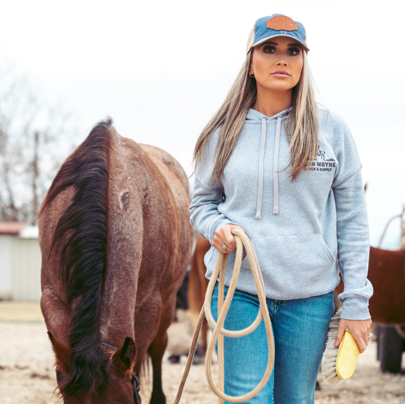 front of woman guiding horse and wearing grey hoodie with john wayne riding horse on pocket