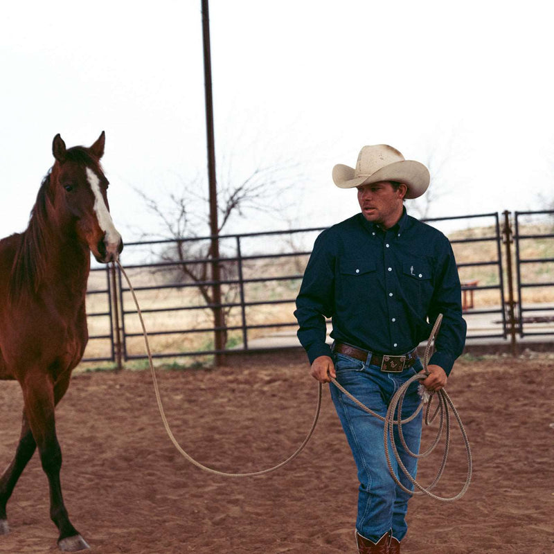 man guiding horse wearing cobalt blue button up long sleeve with john wayne silhouette on left chest pocket