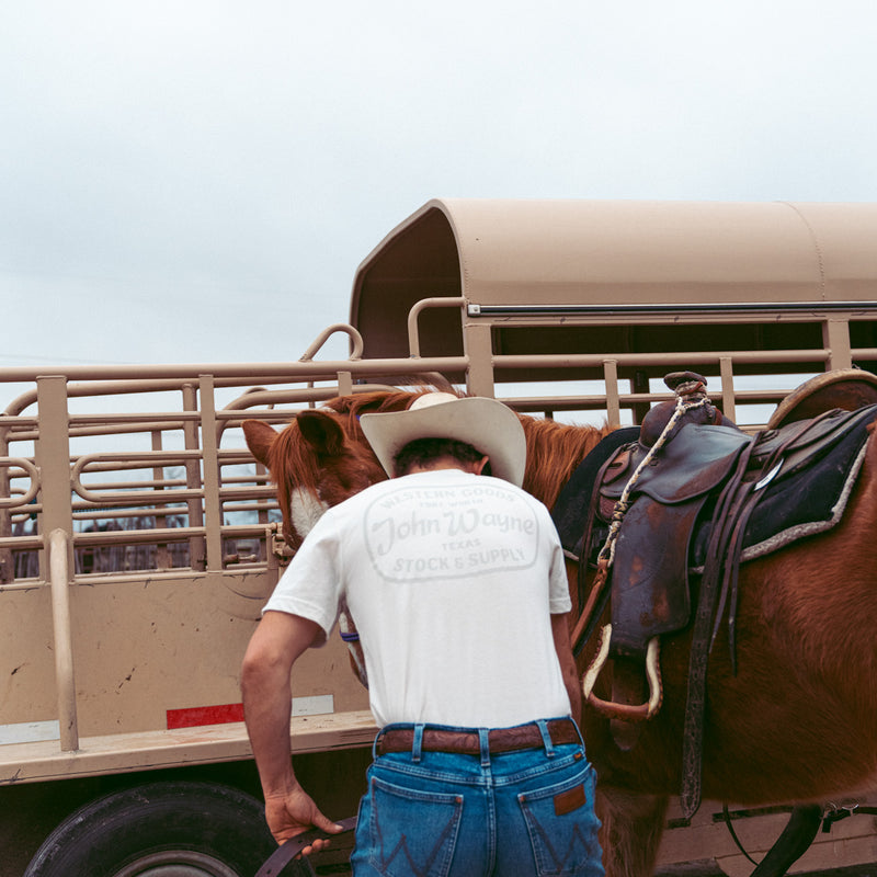 back of man with horse wearing vintage white john wayne western goods fort worth texas tee