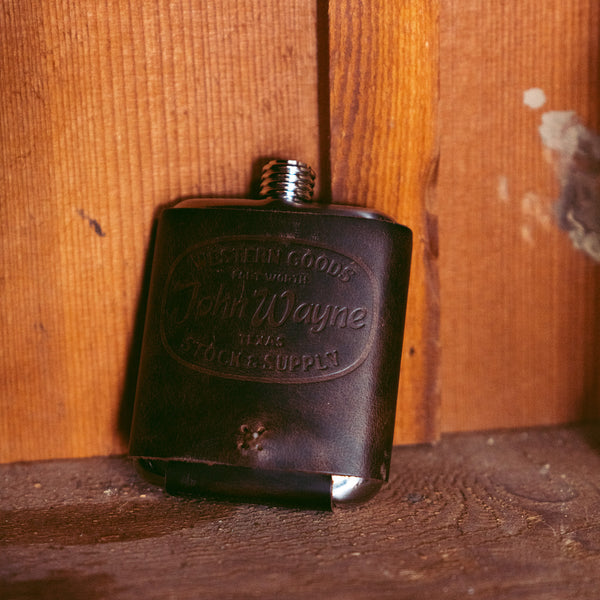 flask with western goods john wayne texas stock & supply leather wrap leaned against wall