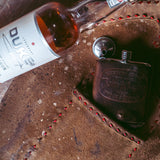 bottle of alcohol next to flask with western goods john wayne texas stock & supply leather wrap