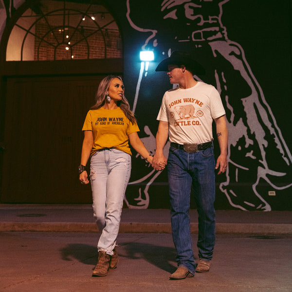 woman and man holding hands with man wearing tee with "john wayne cattle co." and cow design