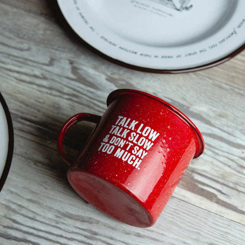 red tin mug laid on table with "talk low talk slow and don't say too much"