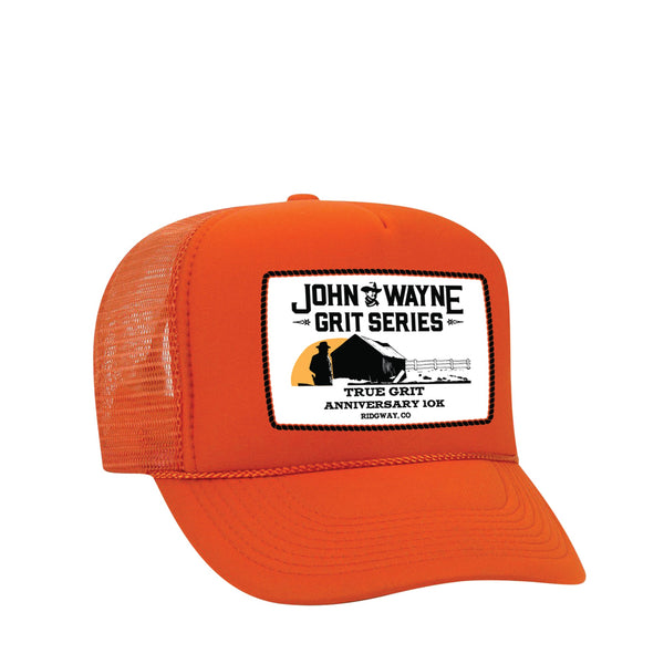 front of orange trucker hat with "john wayne grit series true grit anniversary 10k" and farm scenery