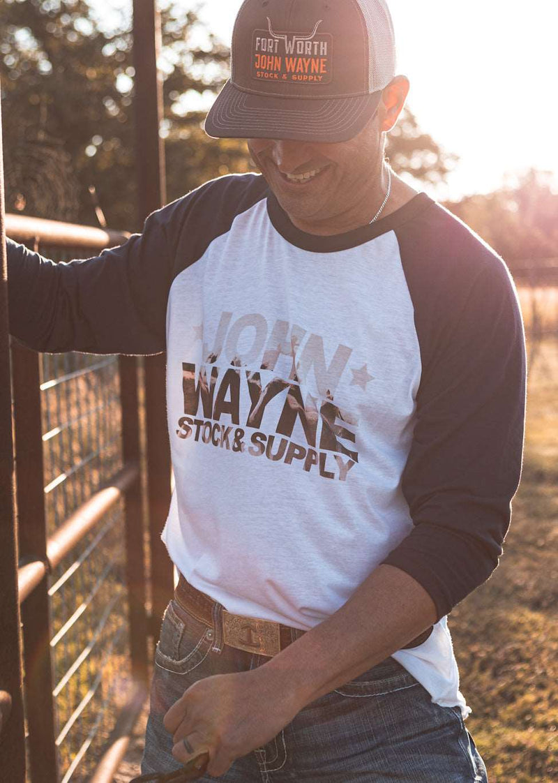 man wearing  john wayne stock & supply raglan with photo of roping cattle in font