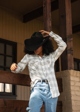 woman standing in cowboy hat and heather grey/white plaid womens woven long sleeve with john wayne silhouette on left chest pocket