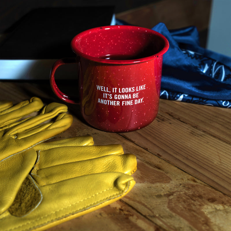red mug with "well, it looks like it's gonna be another fine day" in white font on it sitting on wood table 